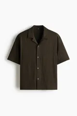 Camisa de manga corta H&M con cuello abierto, confeccionada en tejido de punto con textura. Presenta un diseño de corte holgado con bajo recto y aberturas laterales.