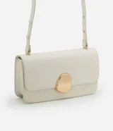 Cartera tipo shoulder bag de tamaño mediano, confeccionada en poliuretano color marrón oscuro. Presenta una solapa frontal con un detalle metálico dorado de forma orgánica y asa ajustable.