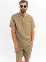 Camisa de manga corta color beige, con cuello mao, cierre frontal parcial con botones y un bolsillo aplicado en el pecho.