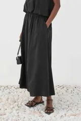 Falda maxi color negro con cintura elástica fruncida y silueta evasé, confeccionada en tejido con textura de motivo geométrico.