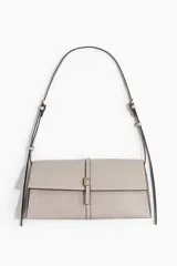 Cartera de hombro tipo sobre, color gris claro, con textura de piel de cocodrilo en relieve. Presenta una solapa frontal asegurada por una tira decorativa con hebilla metálica dorada. Incluye una correa ajustable fina para llevar al hombro.