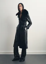 Abrigo largo de estilo trench confeccionado en cuero sintético negro, con diseño recto, cuello con solapa y detalle de cuello de pelo sintético extraíble. Cuenta con cierre frontal de botones, cinturón ajustable con hebilla, bolsillos laterales y mangas largas con trabillas.