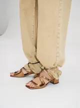 Sandalias de cuero con acabado charol color bronce, con diseño de tiras cruzadas en el empeine, cierre con hebilla ajustable al tobillo y taco cuadrado de 4,5 cm.