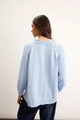 Sweater de punto color marfil con diseño de velero en la parte frontal, cuello con capucha y cordón rojo de ajuste.
