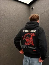Canguro negro de corte regular con capucha y bolsillo frontal. Presenta un estampado gráfico en la espalda en color rojo y crema que incluye una mano sosteniendo una cadena, el título 'Oktubre' y un listado de canciones.