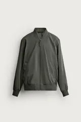 Cazadora bomber de tejido técnico ligero color marrón oscuro, con corte regular fit, cuello, puños y ruedo de rib elástico, bolsillos frontales de vivo y cierre frontal con cremallera.
