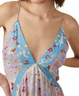 Vestido largo de tirantes finos con estampado floral en tonos lila, rojo y blanco. Presenta escote en V con ribete azul y corte asimétrico en el bajo.