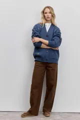 Cardigan de punto azul con cuello en V, cierre frontal de botones y bolsillos delanteros. Presenta bordados decorativos con motivos variados y frases en colores contrastantes.