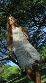 Vestido corto color crudo, con cuello halter y diseño cubierto íntegramente de flecos con lentejuelas.