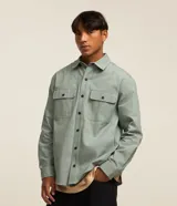 Camisa manga larga de sarga en color verde militar, con cuello inglés, cierre frontal de botones negros y dos bolsillos con solapa en el pecho.