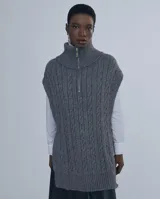 Chaleco largo de punto trenzado color gris con cuello alto y cierre frontal con cremallera metálica.