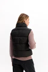 Chaleco matelaseado de color negro, con cuello alto, cierre frontal con broches y diseño acolchado con volumen.