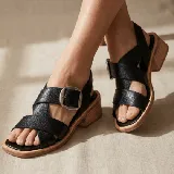 Sandalias de cuero vacuno negro con diseño de tiras cruzadas y hebilla metálica lateral. Presentan una punta cuadrada y un taco bajo de madera.