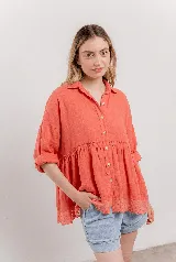 Blusa de lino color coral con corte evasé, caída fluida, mangas relajadas y botones frontales. Presenta un detalle de bordado calado en el dobladillo.
