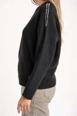 Sweater de lana color negro, de corte oversize, con cuello redondo, mangas largas y detalle de apliques metálicos en los hombros.