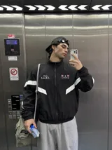 Campera deportiva negra con cuello alto, cierre frontal completo y franjas blancas en las mangas. Presenta estampados en color rosado en el pecho, incluyendo la inscripción "Only F.A.N.S." y gráficos de palmeras con estrellas.