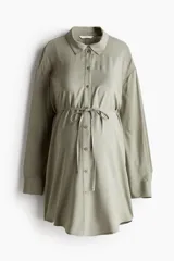Camisa tipo túnica color verde militar, con cuello camisero y cierre frontal de botones. Cuenta con mangas largas de hombros caídos, puños abotonados, bajo redondeado y un cordón fino para atar en la cintura.