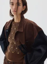 Campera tipo trucker de corte oversize, confeccionada en algodón con diseño colorblock en tonos azul marino y bordó. Presenta cierre frontal con botones metálicos, cuello clásico y bolsillos frontales con solapa.