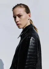 Chaqueta corta de cuero negro con textura efecto cocodrilo, diseño recto, cuello camisero, manga larga, bolsillos laterales de ribete y cierre de doble botonadura.