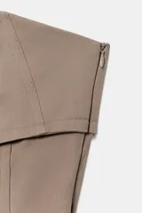 Vestido mini taupe de escote palabra de honor y hombros descubiertos, con detalle de tejido superpuesto y tiras cruzadas ajustables en el pecho. Cuenta con cierre lateral con cremallera oculta.