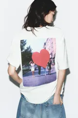 Camiseta de algodón color blanco hueso, corte regular, con cuello redondo y manga corta. Presenta un estampado pequeño en color rojo oscuro en el pecho con el texto "Action Heart Object" y detalles adicionales.