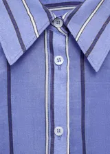 Camisa celeste con rayas verticales blancas y grises, de corte oversize, cuello camisero y mangas largas con puños abotonados.