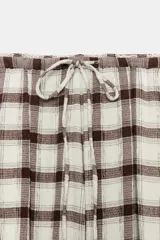 Pantalón bombacho de tiro alto con estampado de cuadros en tonos crudo y marrón. Presenta cintura elástica ajustable con cordón y bajos elásticos.