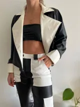 Chaqueta de cuero sintético negra con detalles en blanco, de corte recto y solapas amplias. Incluye un top bandeau negro y un pantalón bicolor de cuero sintético negro y blanco.