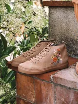 Botín de cuero serraje color beige, con cordones y detalle de flores bordadas en el lateral. Cuenta con suela plana de goma y cierre de cremallera lateral.