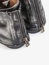 Bota corta de cuero bovino negro con efecto desgastado y envejecido, con detalles en gris claro. Presenta un diseño con solapa frontal que se ajusta con un broche y una cremallera lateral expuesta en el talón. Posee un taco bajo y cuadrado.