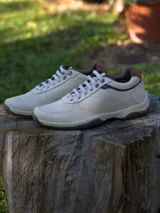 Zapatillas de cuero color beige con cordones blancos, detalles en marrón y suela marrón.