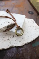 Collar choker artesanal con cordón de cuero marrón y dije circular metálico dorado.