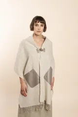 Chal de lana fina sin teñir con diseño de cuadros sutiles, cierre frontal con alamar y bolsillos de cuero metalizado. Presenta terminaciones con flecos en el ruedo y un calce estructurado en los hombros.