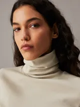 Top color crema de algodón con textura de canalé, corte slim, largo cropped, cuello alto y manga larga.