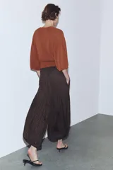 Pantalón de tiro medio con diseño bombacho, confeccionado en tejido con textura plisada y estampado de cuadros vichy en tonos oscuros. Presenta cintura elástica con cordón ajustable y bajos con puños elásticos.