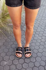 Sandalias bajas de cuero color marrón con tiras de cuero charol negro y hebilla metálica.