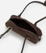 Cartera tipo shoulder bag de tamaño pequeño y formato alargado, confeccionada en material sintético efecto gamuza. Cuenta con asas de hombro estructuradas, cierre superior con cremallera y detalles metálicos decorativos.