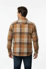 Sobrecamisa de franela a cuadros en tonos marrones, blancos y rojos, con mangas largas, bolsillos frontales con solapa y cierre de botones.