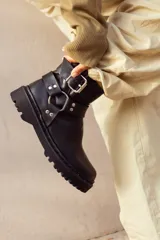 Bota corta negra de cuero sintético con suela track, caña baja y correas con hebillas metálicas.