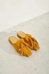 Zueco plano de cuero color dorado, con diseño de tiras anchas entrelazadas en el empeine y punta cuadrada.
