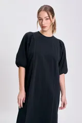 Vestido negro de corte recto y largo midi, con cuello redondo y mangas globo cortas. Presenta pespuntes contrastantes en color claro que recorren el frente y los hombros.
