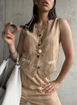 Chaleco beige con estampado de rombos blancos, cuello en V, cierre con botones y bolsillos delanteros ribeteados.