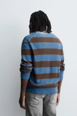 Jersey de punto de algodón con ajuste relajado, cuello redondo y manga larga. Presenta un diseño de rayas horizontales en azul y marrón, con detalles de efecto desgastado y roturas en el cuello, puños y bajo.