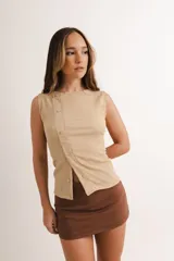 Remera color beige de tejido texturizado, sin mangas, con cuello redondo y cierre frontal asimétrico con botones.