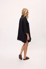 Vestido camisero negro de algodón, con mangas tres cuartos y cuello camisero. Presenta detalles de costura en zigzag color naranja en el cuello y en los puños.