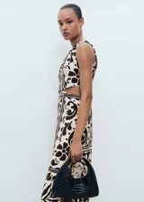 Vestido midi sin mangas con cuello redondo y aberturas laterales tipo cut-out en la cintura. Presenta un diseño recto con estampado botánico en contraste y cierre de cremallera en la parte posterior.