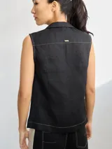 Camisa sin mangas de lino, color blanco, con cuello solapa, cierre frontal con botones y bolsillo pequeño en el pecho. Presenta costuras decorativas a la vista que definen la silueta.