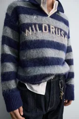 Polo de punto cepillado con diseño de rayas horizontales en azul marino y gris. Presenta cuello solapa con abertura frontal, manga larga y texto bordado en el pecho. Acabados en rib en puños y ruedo.