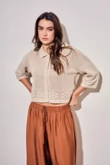 Cardigan de algodón peinado color beige, con cuello camisero, cierre frontal de botones y detalles de textura en crochet con diseño de flores. Mangas tres cuartos y diseño corto.