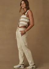 Pantalón deportivo color crema de corte recto con cintura elástica, cordón de ajuste y cinta de rayas plateadas en los laterales.